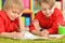 Two smiling boys in red shirts drawing with pencils