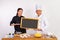 two smiling chefs showing blank blackboard standing near table