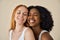 Two smiling diverse cute young girls with eyes closed on beige background.