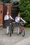 Two smiling girls with school bags walking with bicycles on street