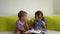 Two Smiling Preschool Toddler Children Read Interesting Book of Fairy Tale On Couch. Siblings Little Twins Look At Each