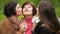 Two smiling sisters are hugging and kissing their mother outdoors. Happy family spending time together in the park.