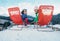 Two smiling skiers sit in chaise-longue on the mountain top