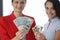 Two smiling women are holding fan of one hundred American dollar bills and credit bank cards.