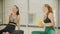 Two smiling women in sport clothes sitting in the gym - drink water from the bottles and talking