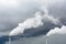 Two smokestacks emitting white smoke against a stormy sky