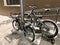 Two snow-covered bikes parked with a tether near a pillar near the ramp near the entrance of the house entrance