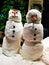 Two snowmen in white with a carrot nose and coal buttons in a store front window.