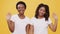 Two sociable African American female friends waving hands to camera and smiling, gesturing hello, yellow background