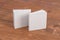 Two softcover or paperback square white mockup books standing on the wooden background. Blank front and back cover