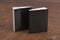 Two softcover or paperback vertical black mockup books standing on the wooden background. Blank front and back cover