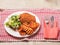 Two southern fried chicken fillets, green fresh salad and fancy cut potato lattice served on a white plate. Poultry meat dinner.