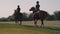 Two sportswomen are riding horses along a field