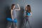 Two sporty women doing handshake while standing with twisted blue rugs against gray empty wall