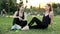 Two sporty women talking while sitting on the grass in city park on sunset, have a break time during the training