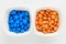 Two squared small bowls with small orange and blue sugar coated chocolate candies isolated on white background, top view or flat l