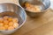 Two stainless steel bowls filled with many cracked eggs with whole yolks, in the wooden table. Close up