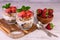 Two strawberry parfaits with yogurt and granola on a white wooden background.