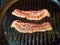 Two strips of bacon frying on a stovetop grill pan