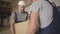 Two strong muscular Caucasian workers taking up heavy cardboard box and carrying it at the construction site. Adult male