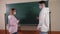 Two students in medical masks stand in a math class near the blackboard and talk