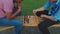 Two students playing chess game sitting on bench outdoors at sunset