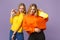 Two stunning young blonde twins sisters girls in vivid clothes, heart eyeglasses hold yellow skateboard  on