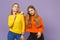 Two stunning young blonde twins sisters girls in vivid colorful clothes standing, looking camera isolated on pastel