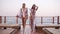 Two stylish caucasian tanned women in similar style clothes walk by wooden floor outdoors on a windy day. Seaside, front