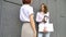 Two successful businesswomen are talking about a the project while standing near the wall outside with a laptop during a