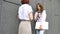 Two successful businesswomen are talking about a the project while standing near the wall outside with a laptop during a