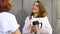 Two successful businesswomen are talking about a the project while standing near the wall outside with a laptop during a