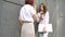Two successful businesswomen are talking about a the project while standing near the wall outside with a laptop during a
