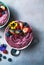 Two summer acai smoothie bowls with strawberries, blueberries, on gray concrete background. Breakfast bowl with fruit and cereal