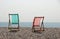 Two sunlit deckchairs on a pebble beach