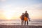 Two surfers hugging stand on sand watching the sunset over ocean