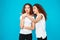 Two surprised girls twins pointing finger away over blue background.