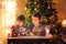 Two sweet boys, brothers, making gingerbread cookies house, decorating at home in front of the Christmas tree