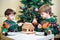 Two sweet boys, brothers, making gingerbread cookies house, decorating at home in front of the Christmas tree, child playing and