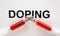 Two syringes filled with red liquid word doping written in capital letters in background