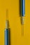 two syringes with a vaccine on a yellow background
