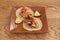 Two tacos of carnitas and vegetables with coriander and a few pieces of lime on an earthenware plate and wooden table