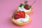 Two tartlets with cream and strawberries on a pink background