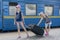 Two teen girls at the train station with a suitcase. Two sisters are pulling a large and heavy black suitcase against the