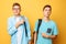 Two teen guys point at each other with their thumbs, blame and do not want to admit their guilt, isolated on a yellow background
