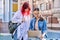 Two teenage female students using outdoor laptop, city street background