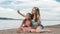 Two teenage are sitting on a sandy beach, on the Internet in phone.