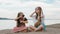 Two teenage are sitting on a sandy beach near the sea. They have two dogs.