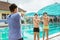 two teenage swimmers in swimming trunks doing arm stretching with trainer