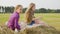 Two teenager girls sitting on hay stack at countryside field in farmland. Happy girls chatting on hay stack at